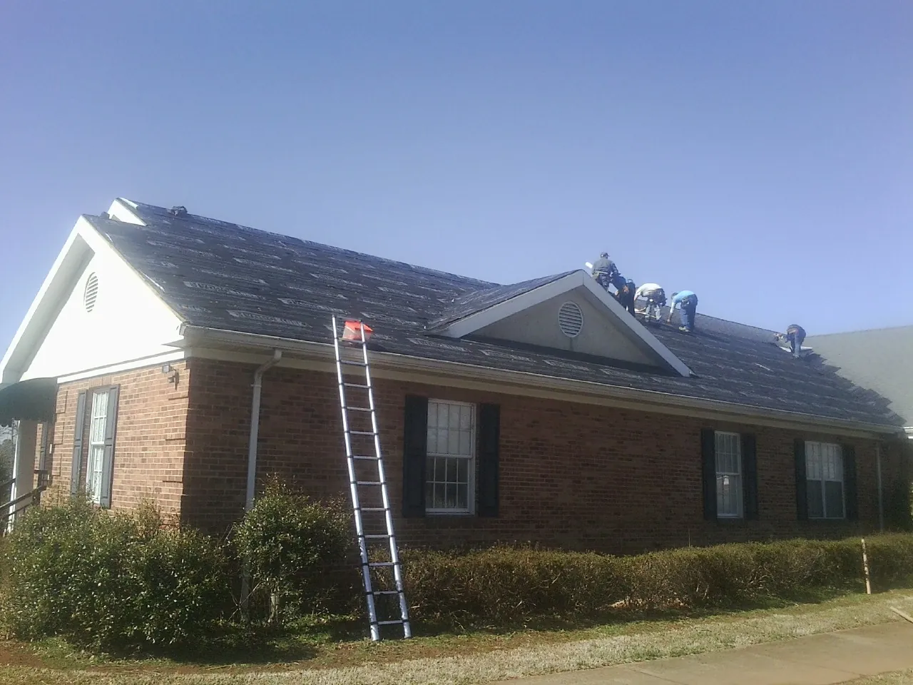 Crew tearing shingles off a brick ranch roof with a ladder set — Metal Roof Repair work by our crew in Fulks Run