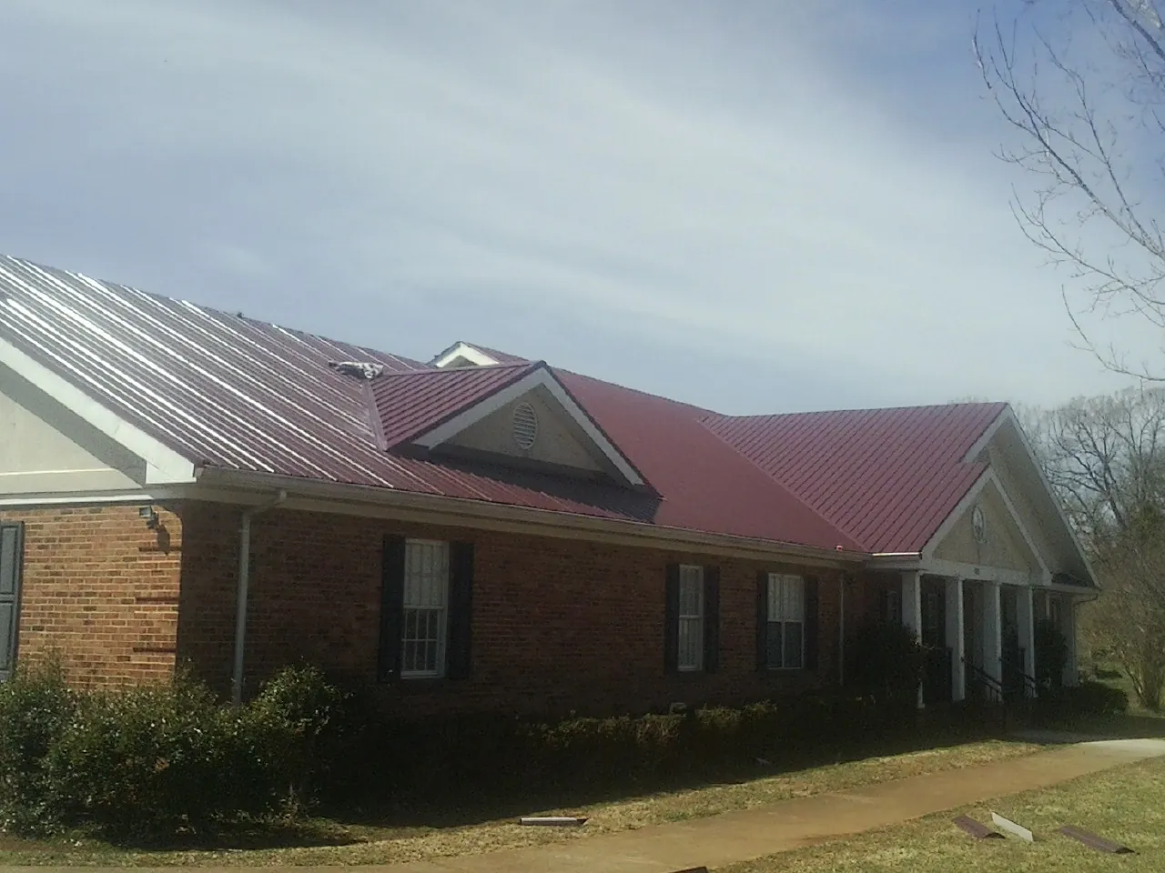 Red metal roof with gabled entries on a long brick building, from a Hail Damage Roof Repair job in Fulks Run