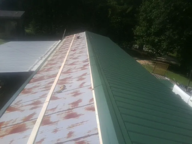 Old rusted panels beside newly installed green metal roofing — Wind Damage Roof Repair by Roofing Brothers in Fulks Run