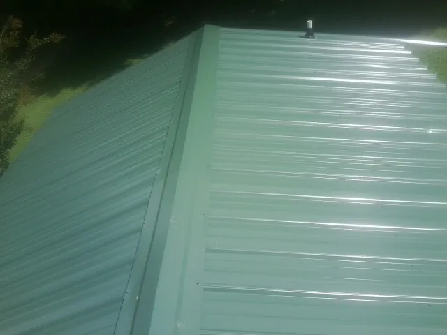 New green metal panels meeting at the ridge of a roof — Flat Roof Repair work by our crew in Fulks Run