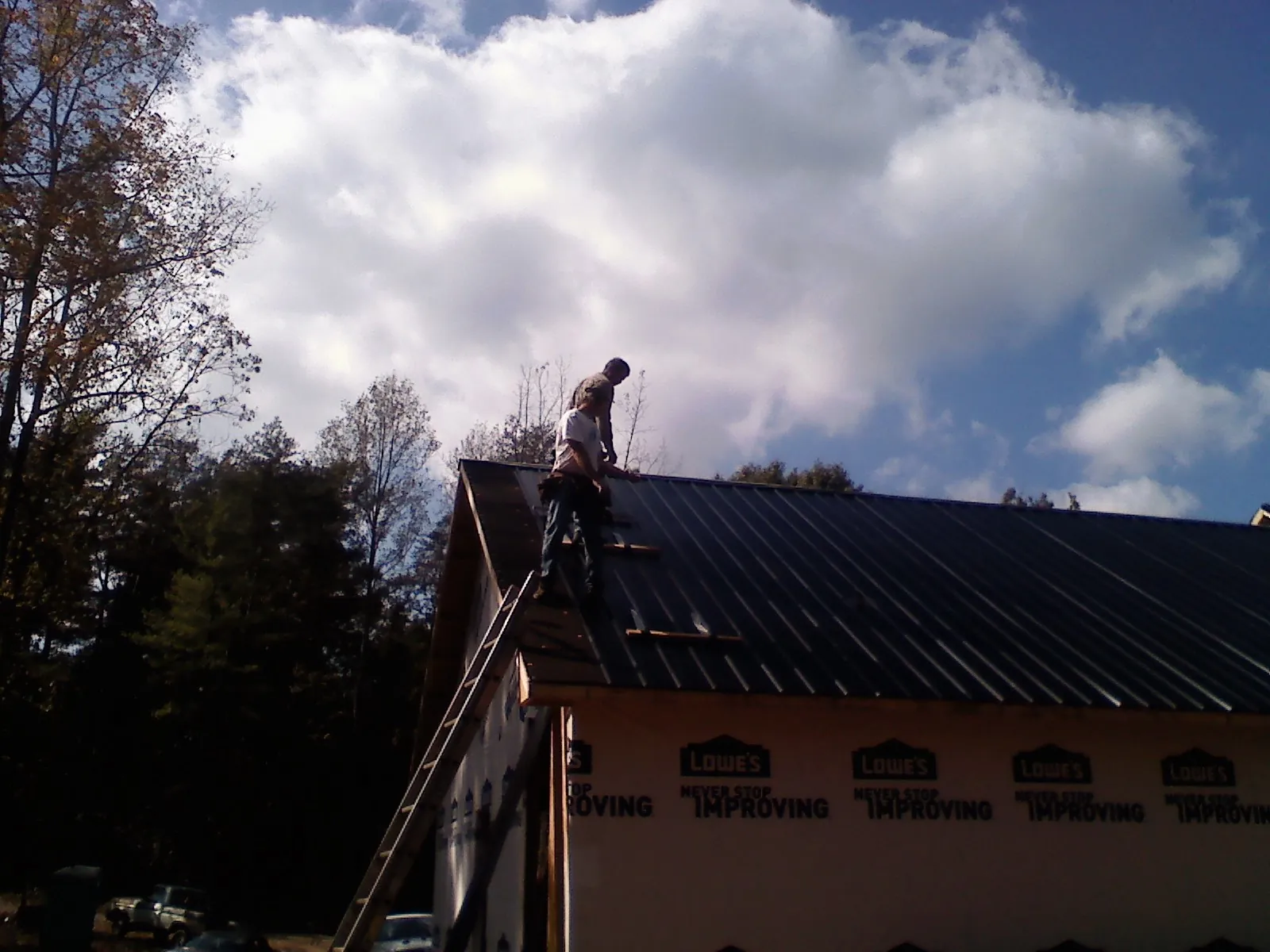 Roofer fastening dark metal panels high against a cloudy sky, from a Roof Inspection job in Fulks Run