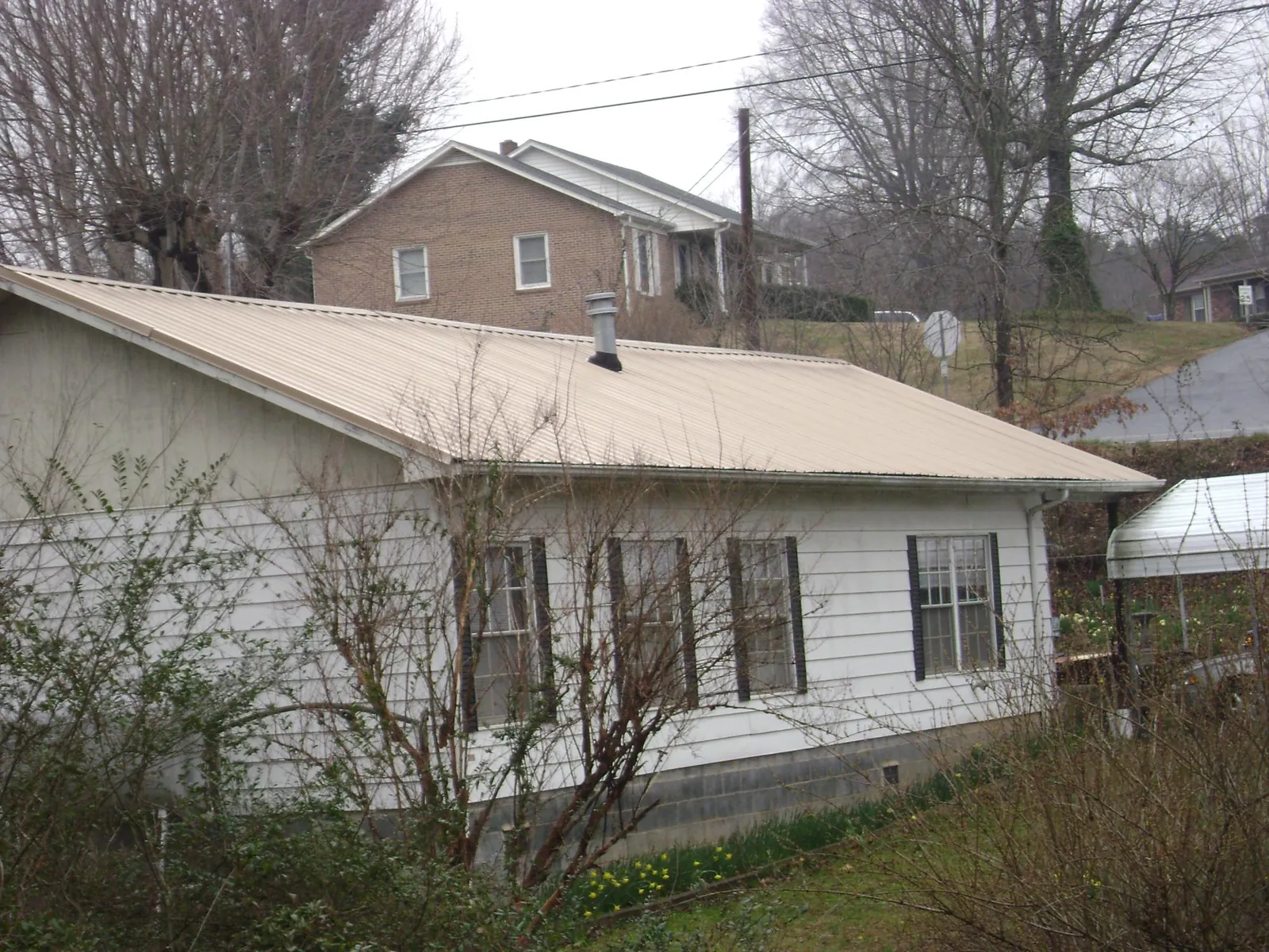 Tan metal roof on a white sided house set into a hillside — Commercial Roofing by Roofing Brothers in Fulks Run